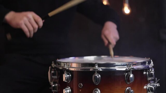 Drummer playing with sticks on a snare drum in the dark slow motion.