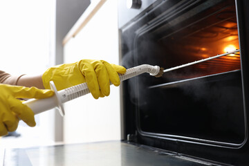 Hands in rubber gloves washing oven with steamer concept - obrazy, fototapety, plakaty