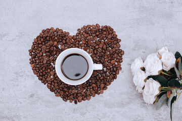 Top view of a cup of coffee on beautiful heart shape from coffee beans with rose flower