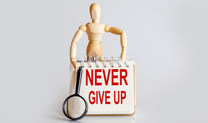 Wooden man shows with a hand to white notepad with text Never give up