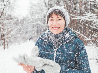 Smiling woman with gloves and knitted hat. Fun in snowy winter forest. Woman laughs as she walks through wood. Sincere emotions.