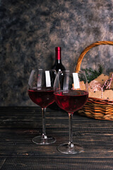 Bottle and glasses of red wine with a gift basket on a wooden table. Gift hamper with boxes, cookies, and Valentine's day ornaments.
