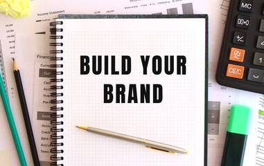 Notepad with text BUILD YOUR BRAND on the office desk, near office supplies. Business concept.