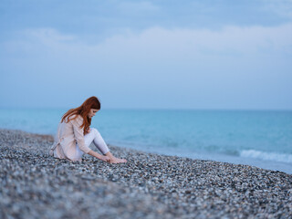 woman in white pants sits on a rocky ocean on the beach