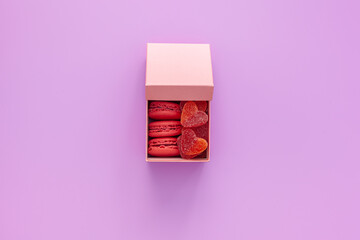 Valentine's day concept. Pink box with marmalade and gift macaroons and a beautiful rose on a pink background