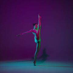 Going on. Young female athlete, rhythmic gymnastics artist dancing, training isolated on purple studio background in neon light. Beautiful girl practicing with equipment. Grace in performance.