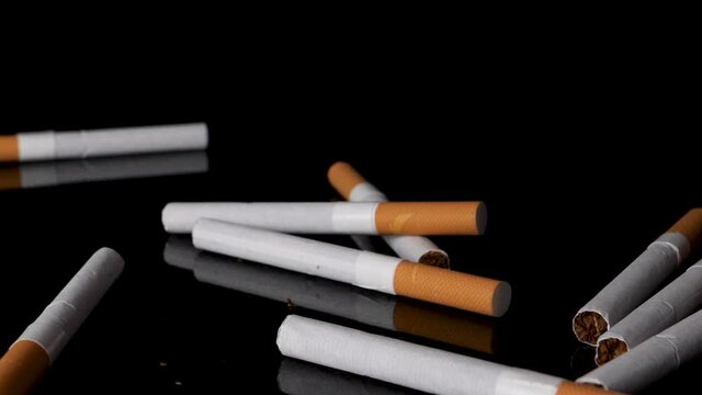 Pile of cigarettes dropping and bouncing on black background in slow motion.
