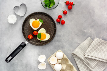Cooking heart-shaped fried eggs in a pan with tomatoes and greens