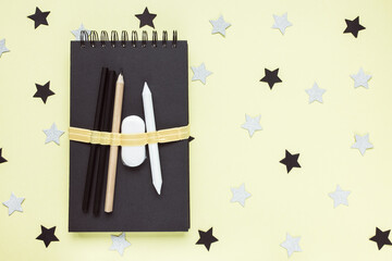 Sketchbook or notebook, charcoal pencils, eraser on desk workspace, yellow with stars background. Creativity, gifts for artist or children and lifestyle concept. Flat lay, top view, copy space