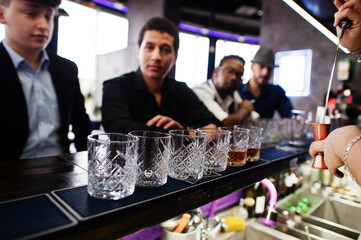 Group of handsome retro well-dressed man gangsters spend time at club. Drinking whiskey at bar counter. Multiethnic male bachelor mafia party in restaurant.