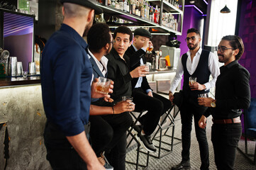Group of handsome retro well-dressed man gangsters spend time at club. Drinking whiskey at bar counter. Multiethnic male bachelor mafia party in restaurant.