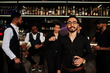 Stylish arab man against group of handsome retro well-dressed guys gangsters spend time at club, drinking on bar counter. Multiethnic male bachelor mafia party in restaurant.