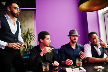 Group of handsome retro well-dressed man gangsters spend time at club, sitting and drinking whiskey. Multiethnic male bachelor mafia party in restaurant.