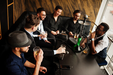 Group of handsome retro well-dressed man gangsters spend time at club, smoking hookah. Multiethnic male bachelor mafia party in restaurant.