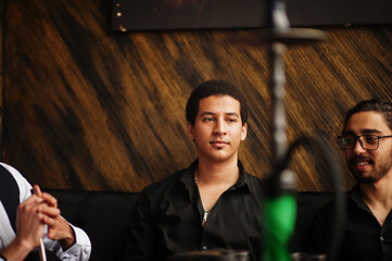 Group of handsome retro well-dressed man gangsters spend time at club, smoking hookah. Multiethnic male bachelor mafia party in restaurant.