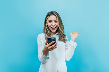 Charming girl on a blue background holds a phone in his hand and looks at the camera in surprise. Place for text