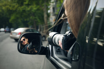 Private detective with camera spying from auto, view through car side mirror