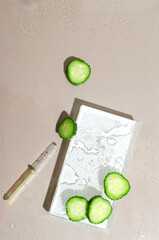 Top view of wet glass stage for product presentation, dropper and pieces of fresh cucumber on the light brown surface