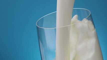 Splash of Pouring milk in glass against blue background, slow motion of flowing cream stream, slow motion - Powered by Adobe