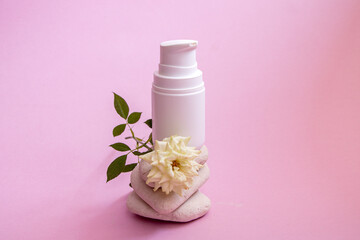 Obraz na płótnie Canvas white plastic jar with dispenser and gentle caring organic hand and body cream, on smooth textured rounded stones on pink background with small room living white rose.