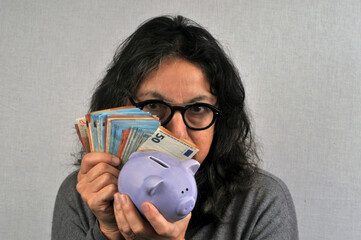Femme radine tenant une tirelire et de billets de banque en main