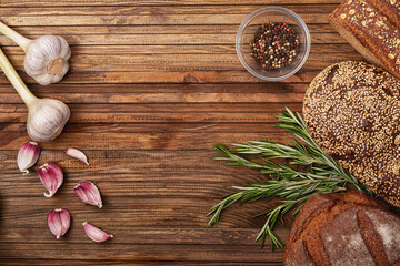 Garlic, cereal bread, rosemary and a plate of pepper mix on a wooden table