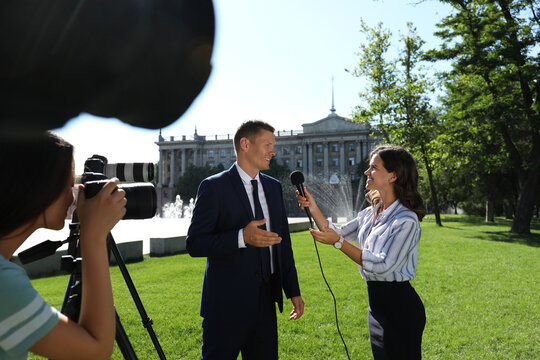 Professional journalist and operator with video camera taking interview outdoors