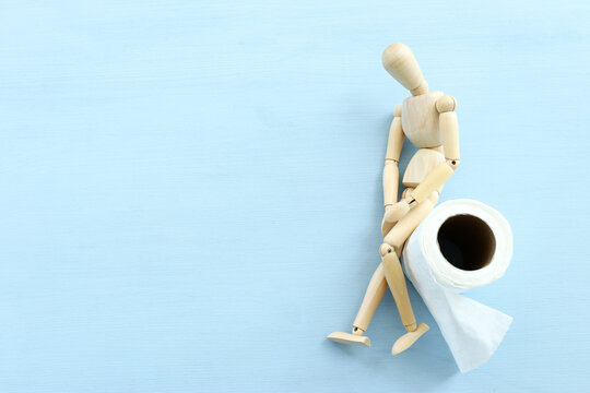 digestion or constipation health problen. Wooden figure sit on a roll of toilet paper. blue background
