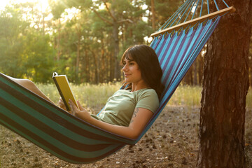 Woman with book resting in comfortable hammock outdoors