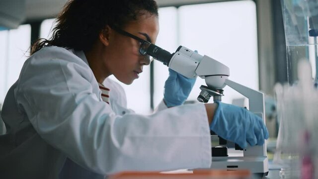 Medical Science Laboratory: Beautiful Black Scientist Looking Under Microscope Does Analysis of Test Sample. Young Biotechnology Specialist, Using Advanced Equipment. Side View Zoom In Portrait