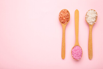 Various types of spa sea salt in wooden spoons on pink background