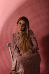 Portrait of beautiful woman sitting on the chair on pink background