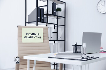 Sheet of paper with words COVID-19 Quarantine on chair in empty office