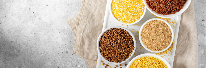 White and red rice, buckwheat, amaranth seeds, corn groats, quinoa and millet in white bowls on the light gray kitchen table. Gluten-free cereals. Top view
