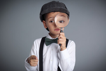 Little boy with magnifying glass playing detective on grey background