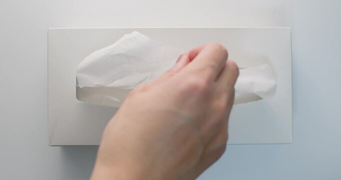 Man hand pull out a piece of tissue from white tissue paper box two time in slow motion from vertical view.
