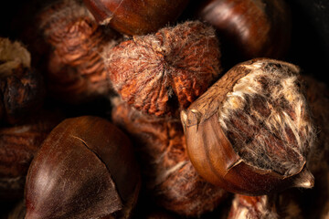 Heap of roasted sweet chestnuts on dark background. Peeled chestnuts and nutshell. Top down view, full frame macro shot. Dark and moody.