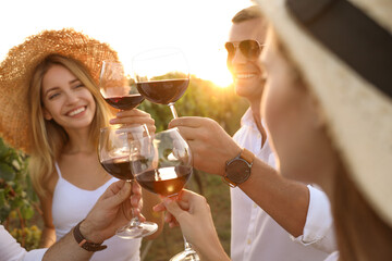 Friends clinking glasses of red wine at vineyard on sunny day, closeup