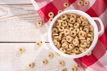 healthy cereal rings on a light wood background with tablecloth red in a plate and scattered on the table with sun rays. morning eat. Healthy children's breakfast. Dry muesli.