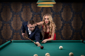 a billiard player is aiming at a ball nearby is a sexy companion watching him