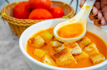 Closeup of human hand taking Tomato Soup with bread croutons in a soup spoon