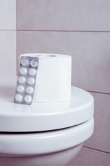 a roll of toilet paper with white pills on the toilet.