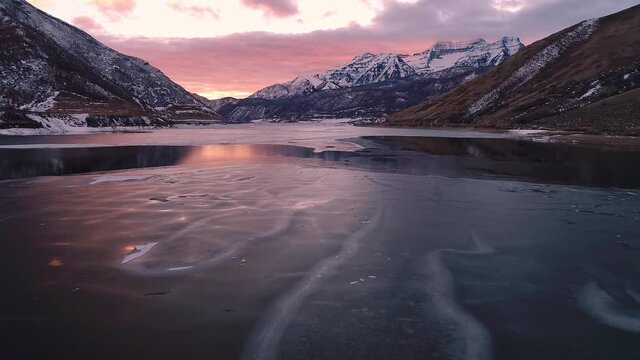 Flying low over ice on lake viewing the texture of the cracks during colorful sunset in Utah.