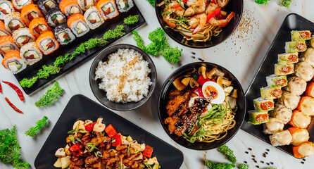 High angle shot of plates with traditional Asian food, seafood, and sushi on a table..