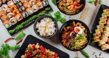 High angle shot of plates with traditional Asian food, seafood, and sushi on a table..