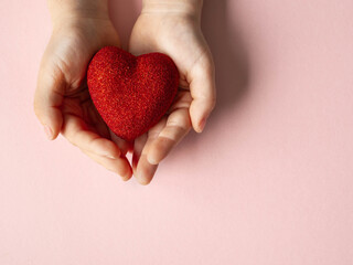 Children's hands are holding a red heart on pink background