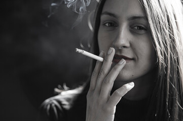 Young woman smoking cigarette on black background