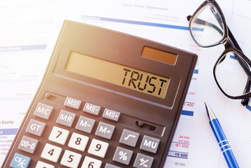 Word TRUST on the display of a calculator on financial documents.