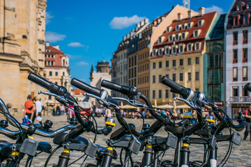 Travel concept photo of rental bikes at Neustadt Square in Dresden. Closeup sharp details of bike and atmospheric bokeh of classic 18th century architecture.  - obrazy, fototapety, plakaty