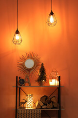 Shelving unit with Christmas decor and firewood near orange wall. Interior design